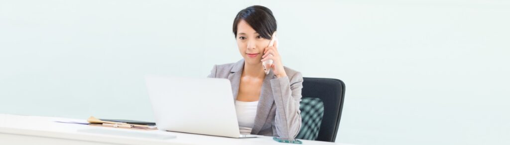 imagem de uma mulher em frente a um computador falando ao telefone para ilustrar conteudo sobre recrutamento e selecao a distancia